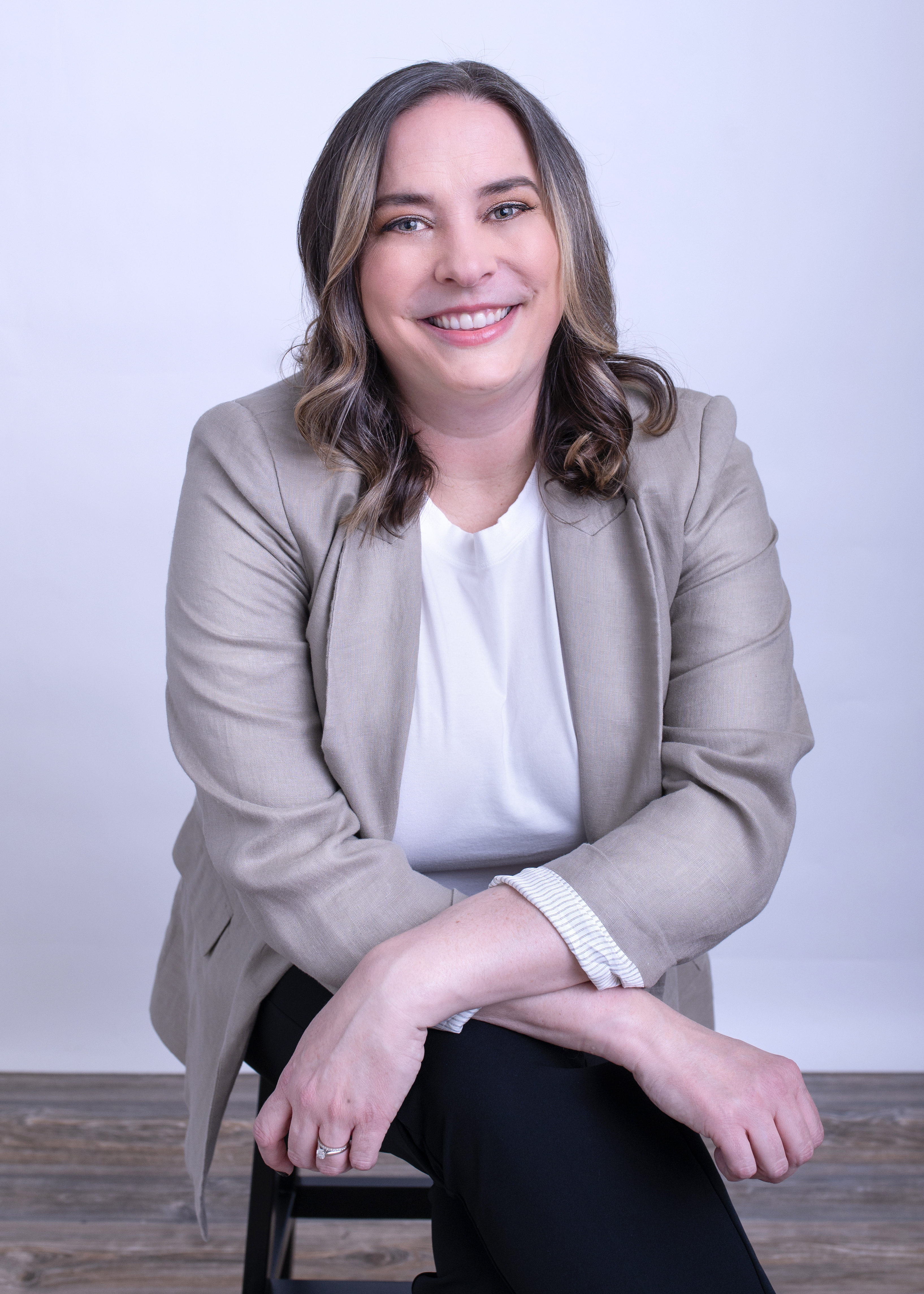 Kate Sonka has long brown hair, and grey blue eyes. She is smiling at the camera and wearing a tan blazer.