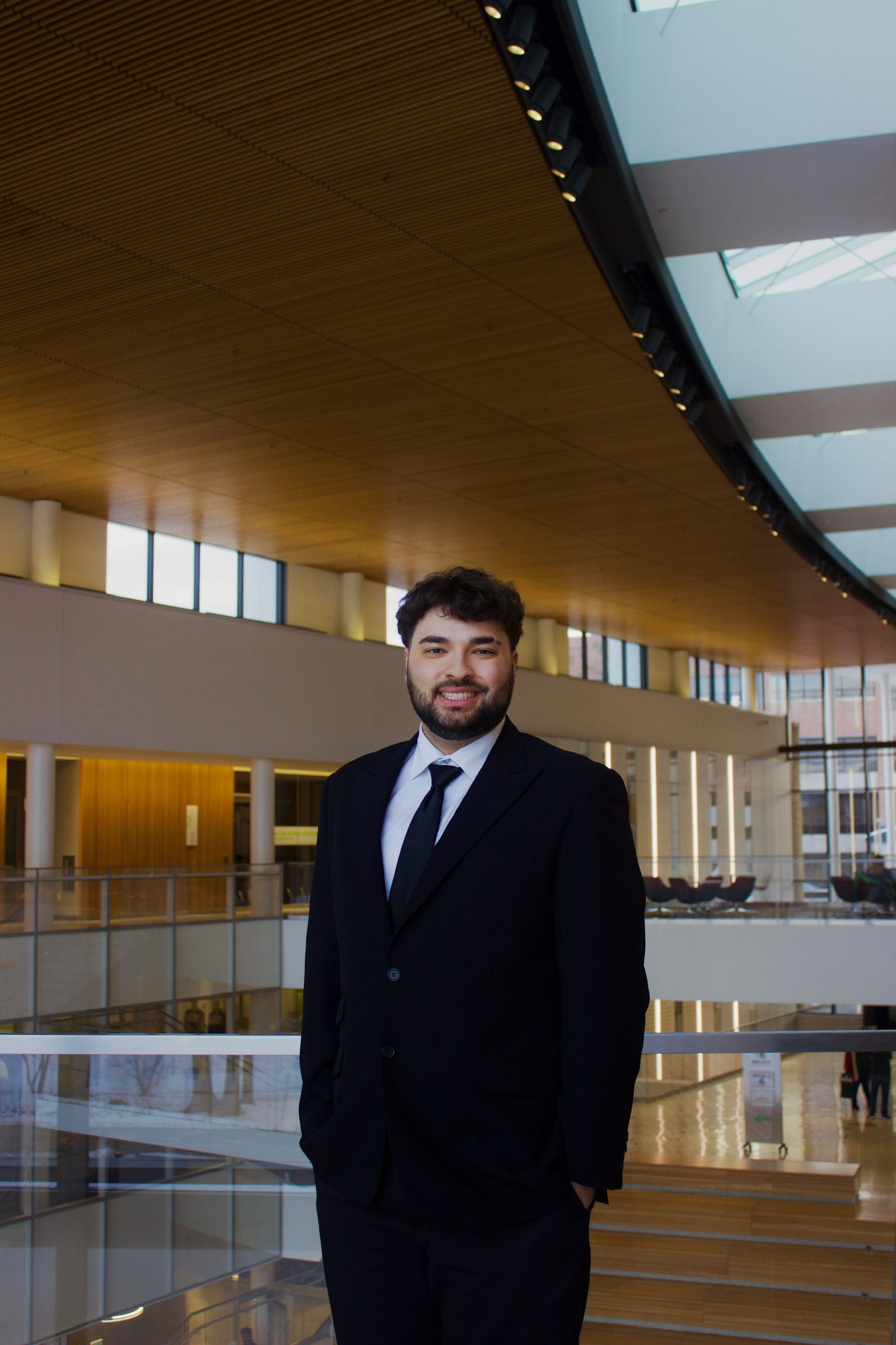 Julius has short dark brown hair and a beard. He is wearing a black suit and is smiling at the camera.